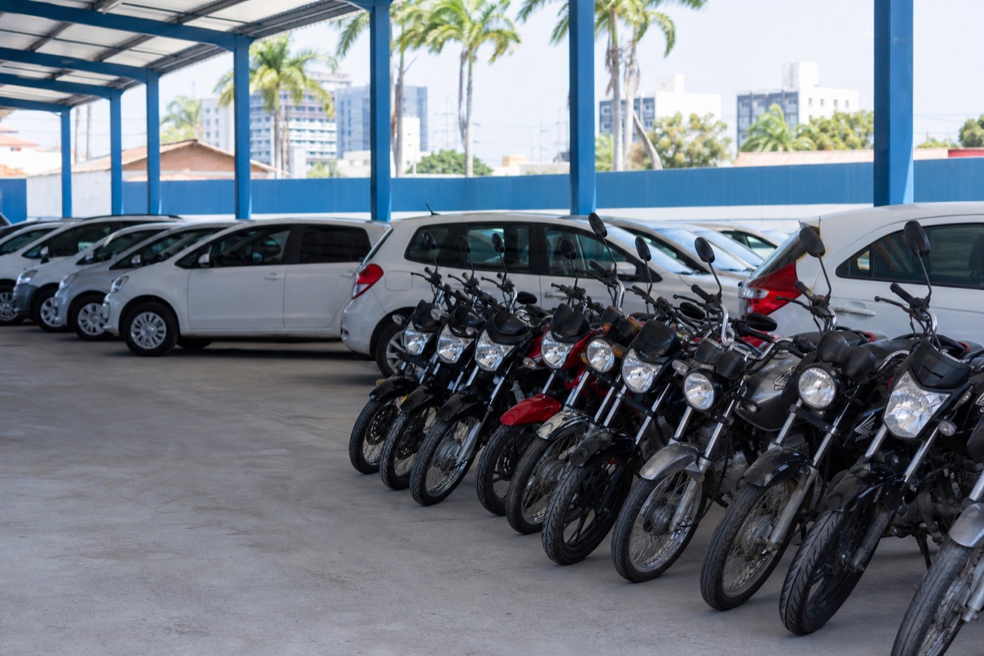 Pátio de locadora com motos e carros sob cobertura